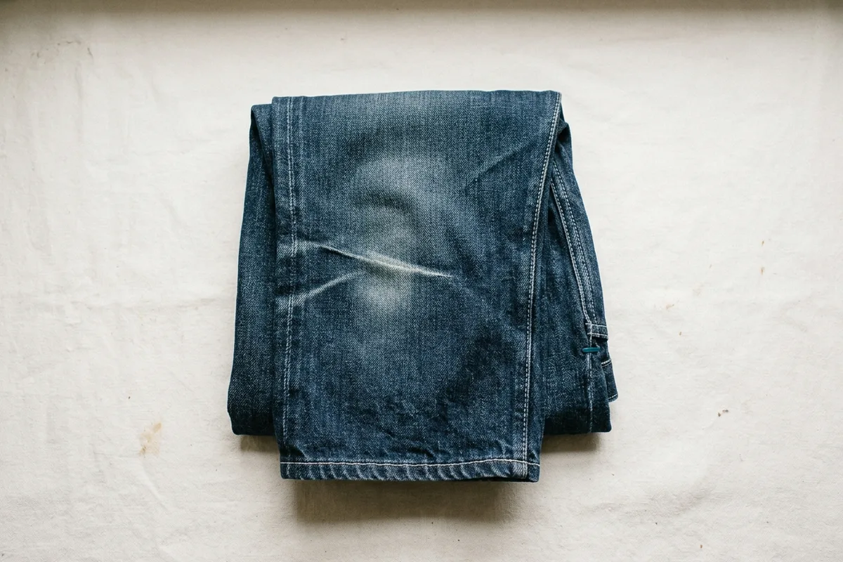 Eine gefaltete Jeans von oben; über dem Knie zeichnet sich eine helle, ausgewaschene Knickfalte ab.